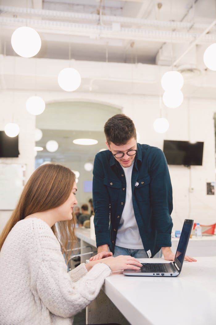 Two young adults collaborating over a laptop in a modern, bright office setting.